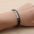 A black and silver personalised leather bracelet worn on a hand, featuring a logo and decorative stitching.