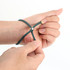 A green metal woven bracelet is being adjusted on a person's wrist, showcasing its flexible design.