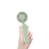 A foldable handheld fan in a soft green colour, held in a hand, featuring a circular fan design and a button.