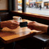 A black metal business card is being exchanged between two hands at a wooden table, with a coffee cup in the background.