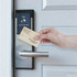 A bamboo business card is being held near a contactless door lock with a sleek silver handle.