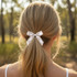 A woman's hair tied in a ponytail with a white elastic hair bow, set against a natural landscape.