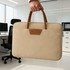 A tan suede PU leather laptop bag with brown handles is being held in an office setting. It features a logo.