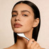 A woman with long, dark hair gently holds a silver facial tool against her jawline, showcasing her natural beauty.
