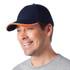 A navy blue cap with an orange accent, featuring a logo, being worn by a smiling man.