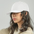 A white cap is worn by a person with wavy hair, featuring a structured brim and a logo on the front.