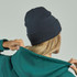 A navy beanie made from recycled polyester worn by a person with long blonde hair, paired with a green hoodie.