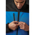 A man zips up a blue and black softshell jacket. The jacket features a high collar and zip pockets.