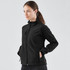 A woman is wearing a black ultra-light shell jacket, featuring a zippered front and side pockets.