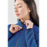 A blue women's full zip jacket with a high collar, featuring a logo and a model adjusting the zipper.