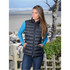 A women's thermal vest in black, featuring a zip front and a fitted design, set against a coastal background.