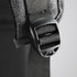 A close-up of a black buckle and strap on a grey backpack, featuring fabric detailing and stitching.