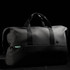 A black duffle bag with dual handles and a logo, featuring a sleek design and spacious interior.