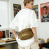 A large brown bum bag attached to a person wearing a white shirt, surrounded by books and basketball memorabilia.