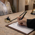 A sleek black and gold pen is being used to sign a document on a reception desk with a gold holder.