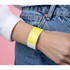 A yellow and white Tyvek adult wristband worn on a wrist, set against a pastel pink background.
