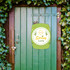 A green wooden signboard with "Spring Party" design, hanging on a wooden door surrounded by ivy.