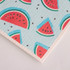 A biodegradable dishwashing cloth featuring a light blue background with red watermelon slice patterns and black seeds.