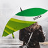 A green and white umbrella with a logo, held by a person with their back turned, against a misty background.