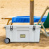 A 120L white cooler box with wheels, positioned on sandy beach by a sun lounger and a blue towel.