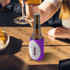 A drink bottle encased in a purple ball shape stubby holder, set on a wooden table with snacks.