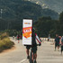 A rectangle backpack flag with a prominent design in red and yellow, displayed on a cyclist on a scenic pathway.