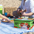 A green sublimation shoulder cooler bag with various designs, sitting on a beach blanket beside food and drinks.
