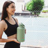 A drink bottle in a muted green colour, held by a woman, featuring a logo and a secure lid design.