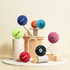 A collection of colourful pet tennis balls in various shades, with some featuring logos, displayed on a minimalistic pedestal.