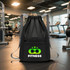 A black drawstring backpack with a fitness logo and adjustable grey straps, set in a gym environment.
