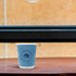 A double wall paper cup in blue, featuring a logo, sits on a wooden table against a textured background.
