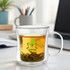 A double wall mug with a clear sleek design, containing green tea and tea leaves, alongside a logo.