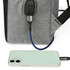 A grey laptop backpack features a USB charging port connected to a phone. The backpack has black accents.