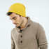 A yellow cable knit beanie worn by a man, with a casual brown sweater and branding on the beanie.