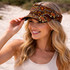 A woman wearing a brown and orange patterned visor, featuring intricate designs, outdoors on a sandy background.