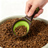 A collapsible pet food scoop with a brown handle and green scoop is being used to lift dog food from a bowl.