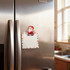 A custom-shaped acrylic magnetic clip in the design of Santa, holding a blank notepad, on a stainless steel fridge.