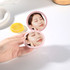 A double-sided round mirror in a pink casing, being held, with a reflection of a person applying skincare.