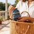 A person holding a small, patterned drawstring bag in shades of blue, with a woven basket nearby.