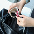A small pocket cosmetic bag in cream, held by a hand, contains several lip products and is inside a black bag.