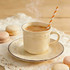 A steaming cup of tea in a decorative cream mug, with a striped orange and white straw, surrounded by pastel macarons.