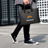 A nylon briefcase in black being carried by a person wearing black jeans and sneakers, featuring a logo.