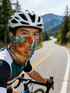 A cyclist wearing a colourful, patterned brushed Lycra warm gaiter, with mountains and a winding road in the background.