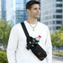 A drink bottle is secured in a black fanny pack, worn across the chest of a person in an urban setting. The pack has a logo.