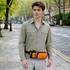 A drink bottle holder fanny pack in orange and black, worn by a man in a green shirt, set on a city street.