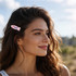 A woman with wavy hair wearing an iridescent pink fish-shaped hair clip against a scenic outdoor background.