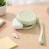 A round silicone pouch in light green, featuring holes, holding wireless earbuds, placed on a wooden surface.