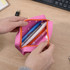 A pink silicone pencil case with an orange zipper, containing various pens and a USB drive inside.