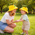 A yellow dinosaur bucket hat with a green dinosaur on top, worn by a woman and a child in a grassy park.