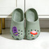 A pair of green clog shoes with colourful charms featuring a mushroom and a purple shoe design, set on a white surface.